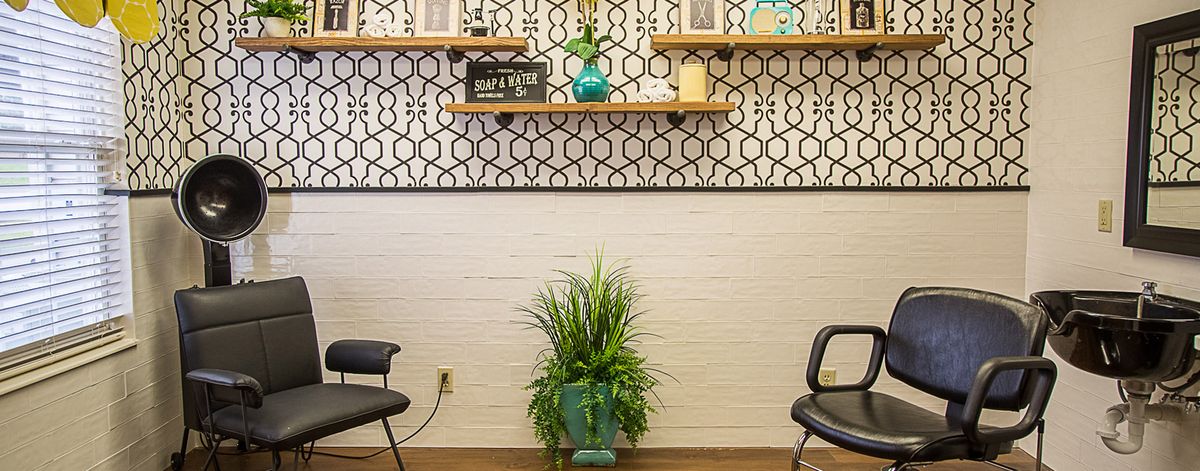 A modern waiting room with decorative shelves, a patterned wallpaper, chairs, and a potted plant.