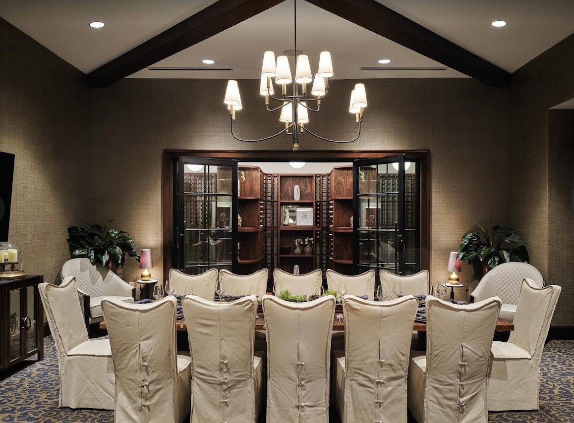 An elegant dining room with upholstered chairs and a classic chandelier, featuring a bookshelf in the background.