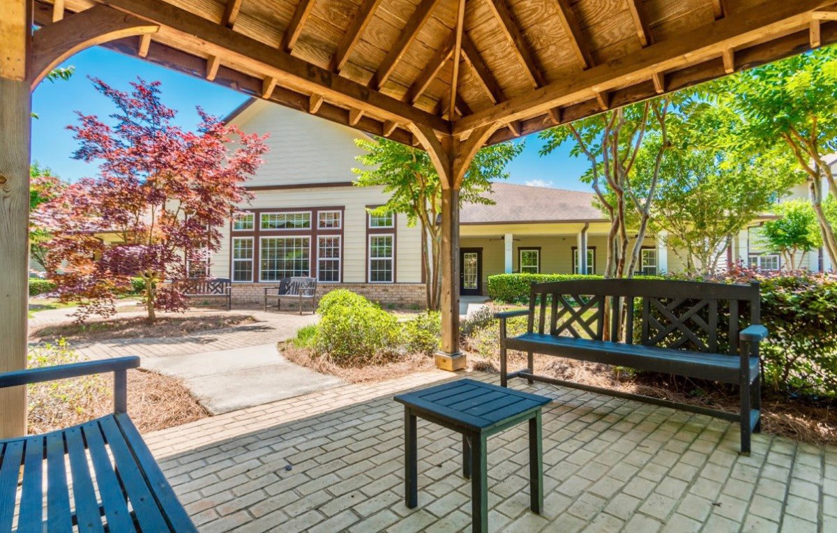 A shaded patio area with benches and a table, surrounded by a landscaped garden.
