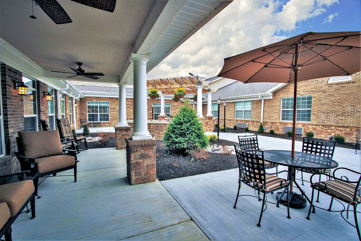 A spacious patio with outdoor seating, shaded by umbrellas, surrounded by a brick building and garden courtyard.