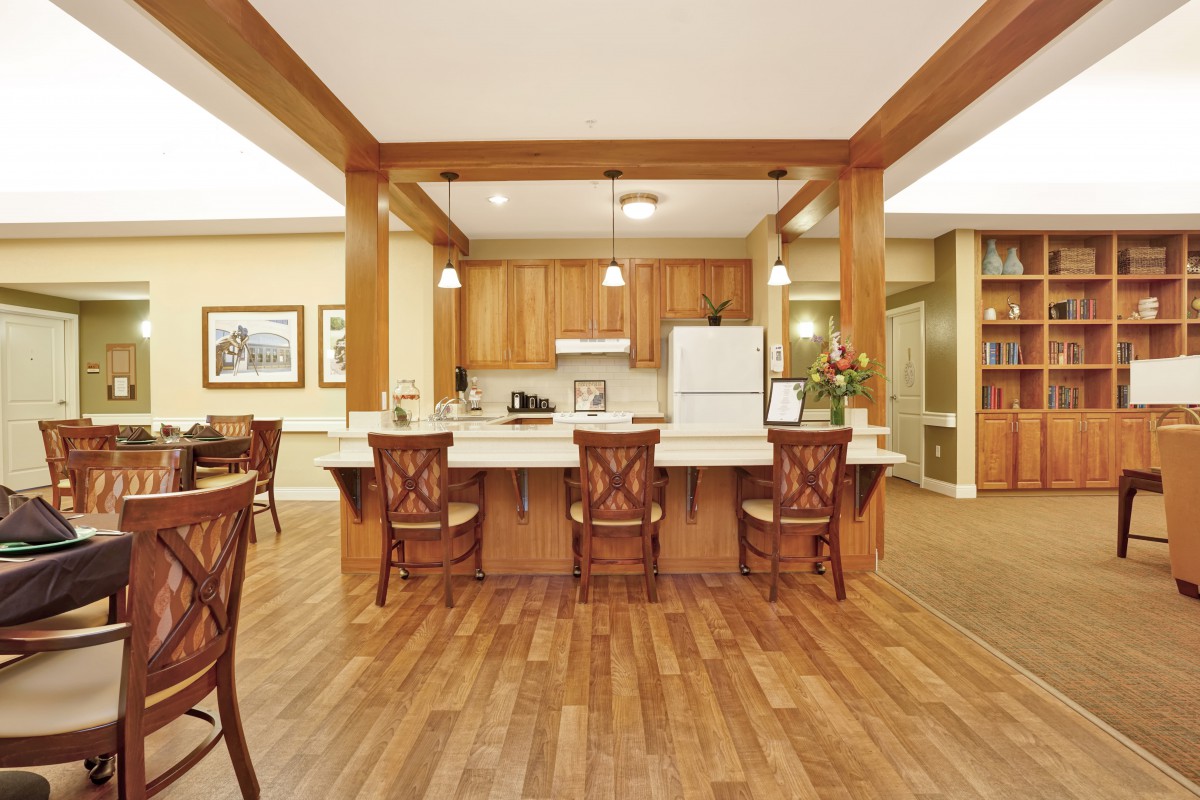 A kitchen with a central island, wooden flooring, and bar stools.