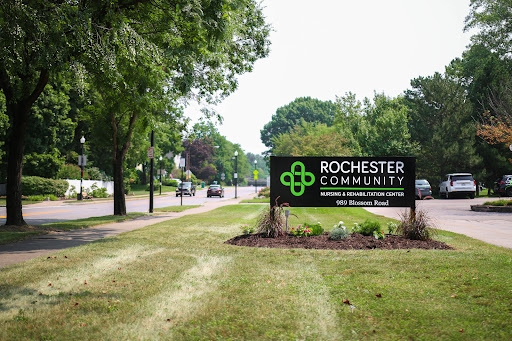 A welcoming sign for Rochester Community set against a lush green landscape.