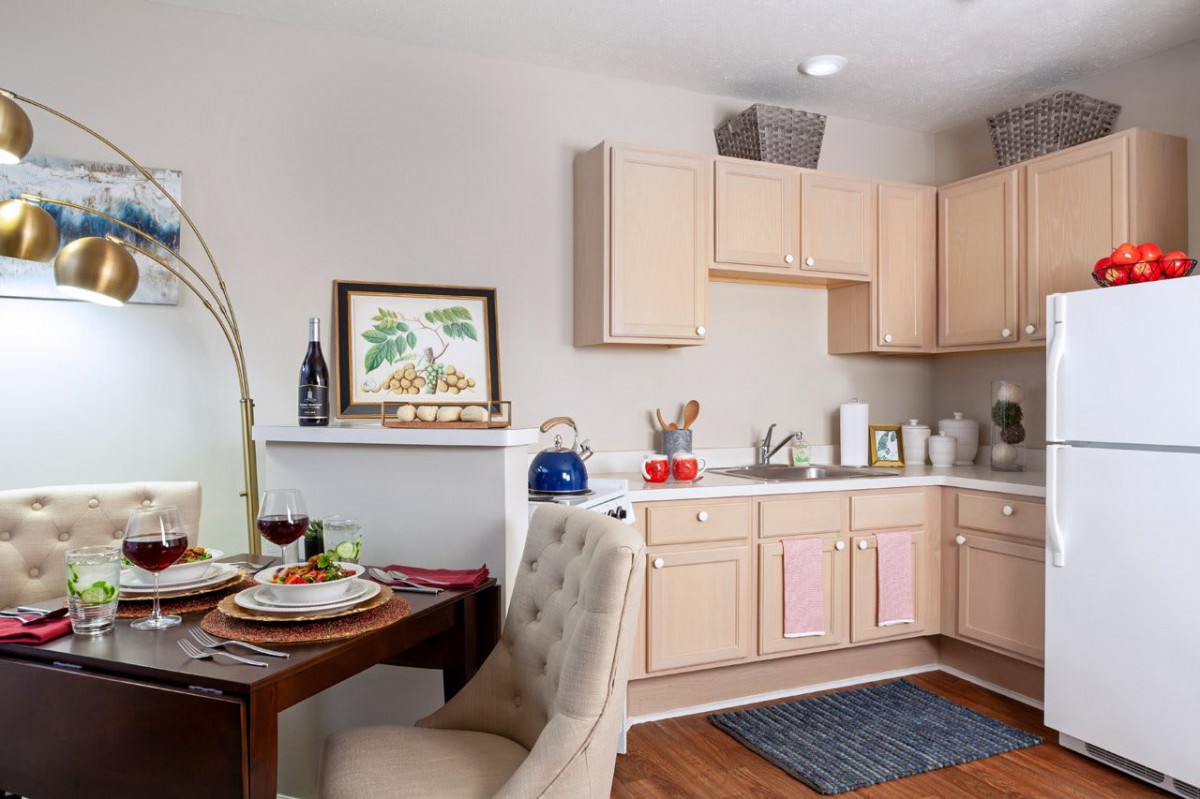 A cozy kitchen and dining area with light wooden cabinets, a small dining table set for two, and decorative elements on the countertop.