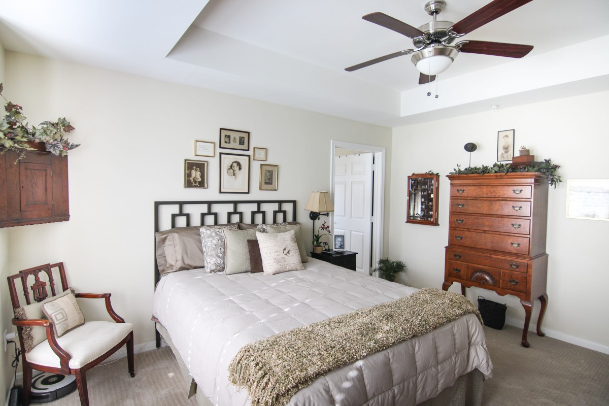 A cozy bedroom featuring a bed with neutral-colored bedding, a ceiling fan, and stylish home decor.