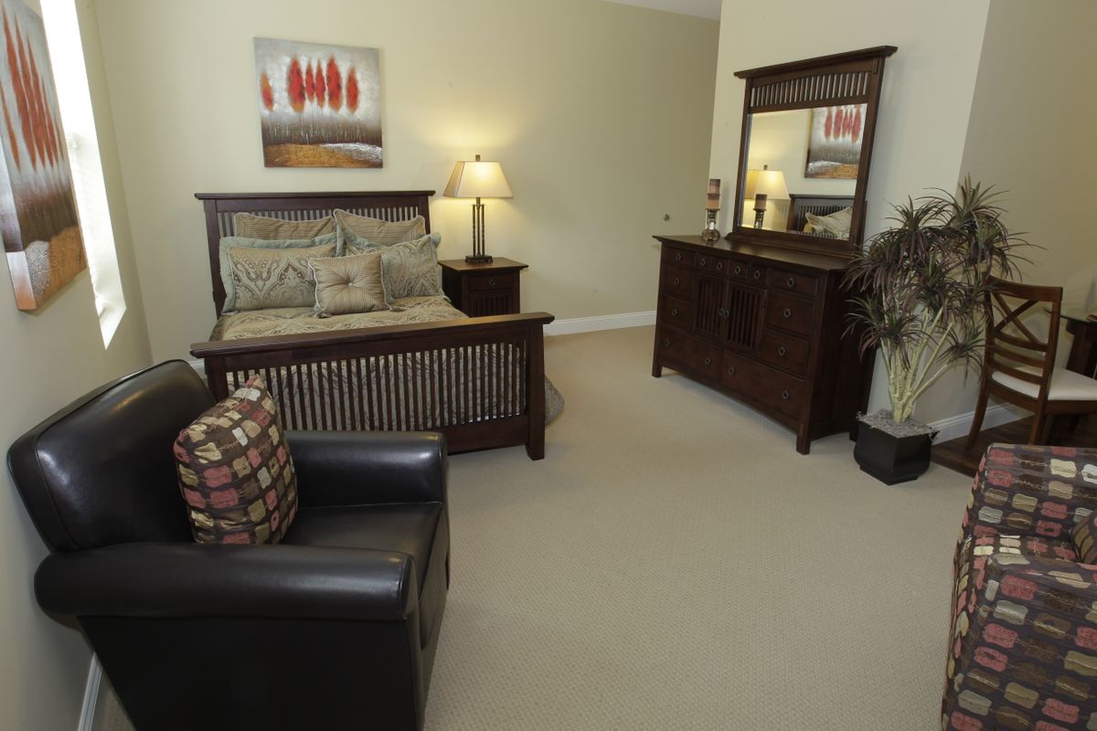 A cozy bedroom with a bed, dresser, mirror, and lamp.