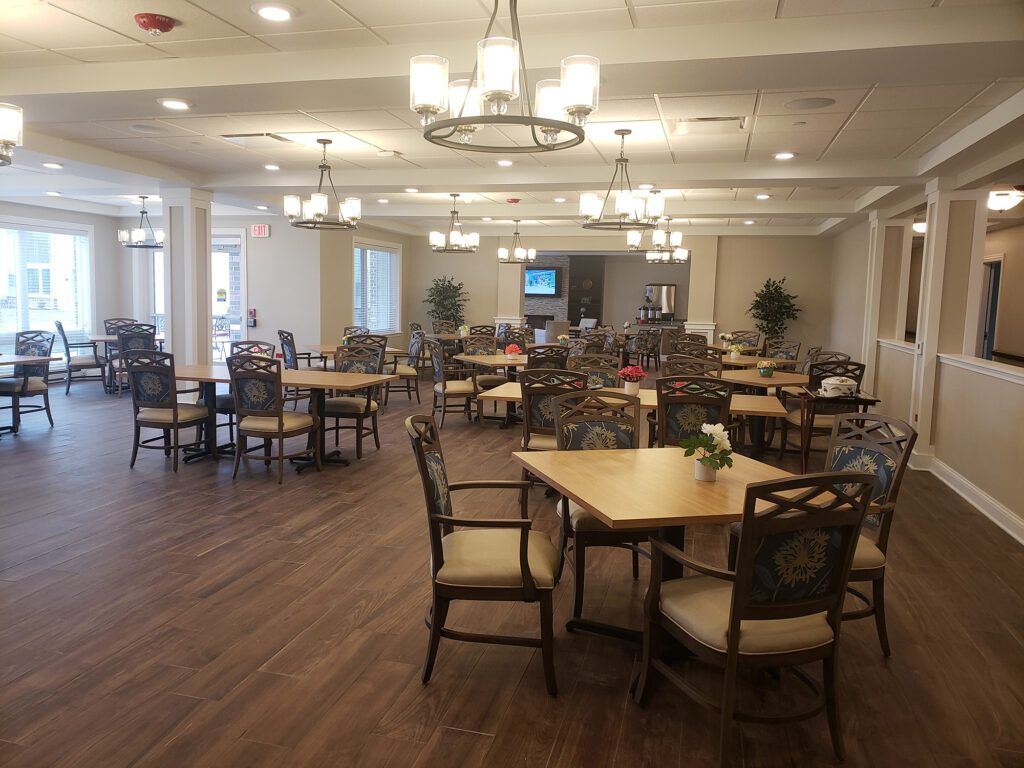 A spacious and elegantly designed dining room with multiple tables and chairs arranged neatly, featuring soft lighting and a wooden floor.