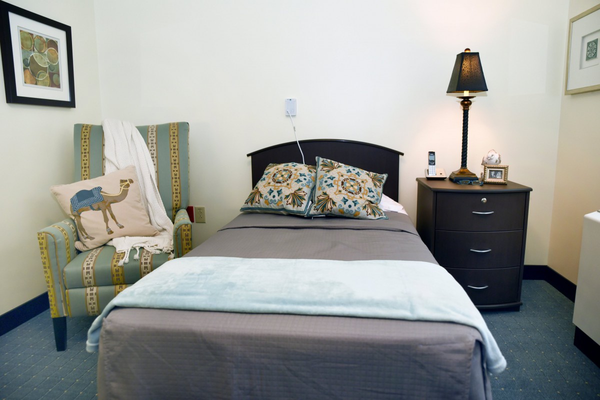 A neatly made bed with patterned pillows, a nightstand with a lamp, and a decorative chair nearby.