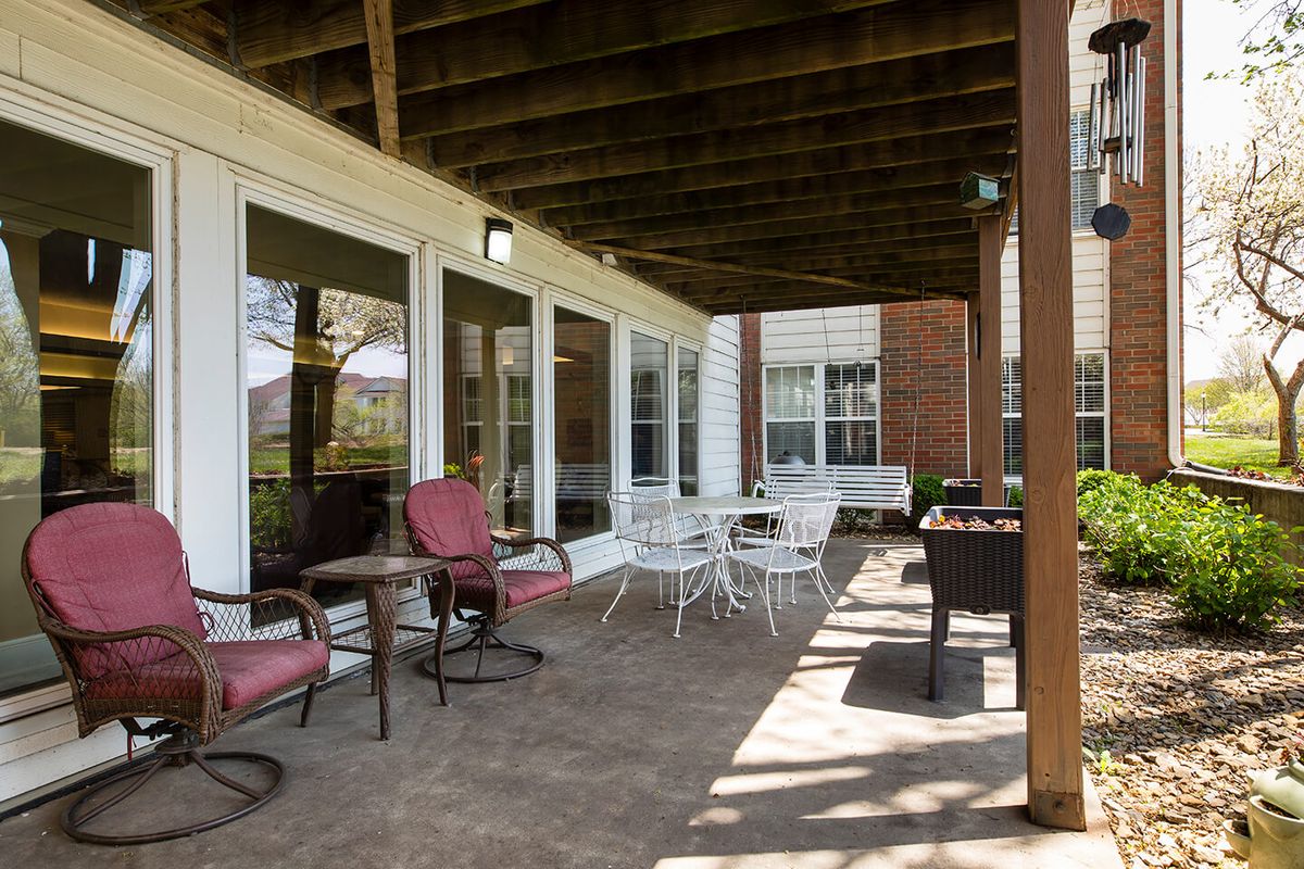 A cozy covered patio featuring outdoor furniture with a brick exterior backdrop.