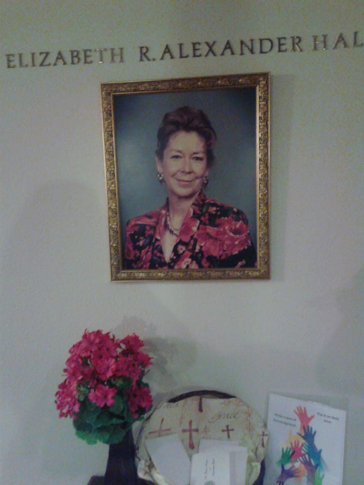 A framed portrait hanging on a wall above a table with flowers.