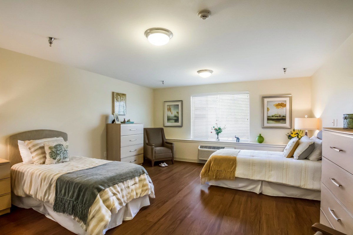 A neatly arranged bedroom with two beds, a dresser, and a chair by the window.