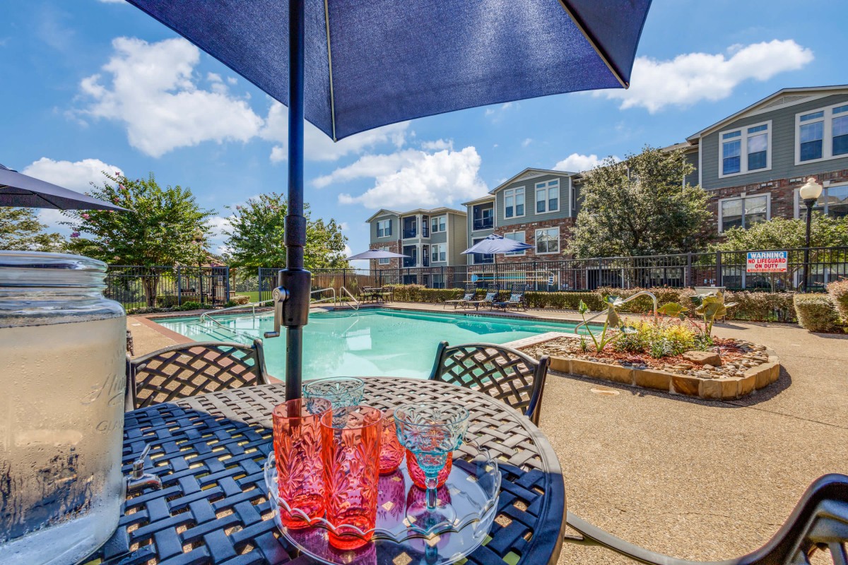 A relaxing outdoor pool area with a table and umbrella on a sunny day.