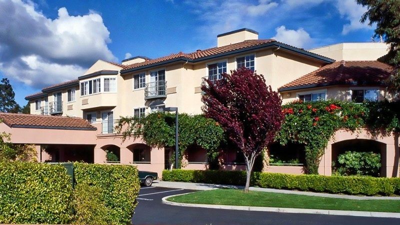 A suburban residential building surrounded by well-maintained landscaping and trees on a sunny day.