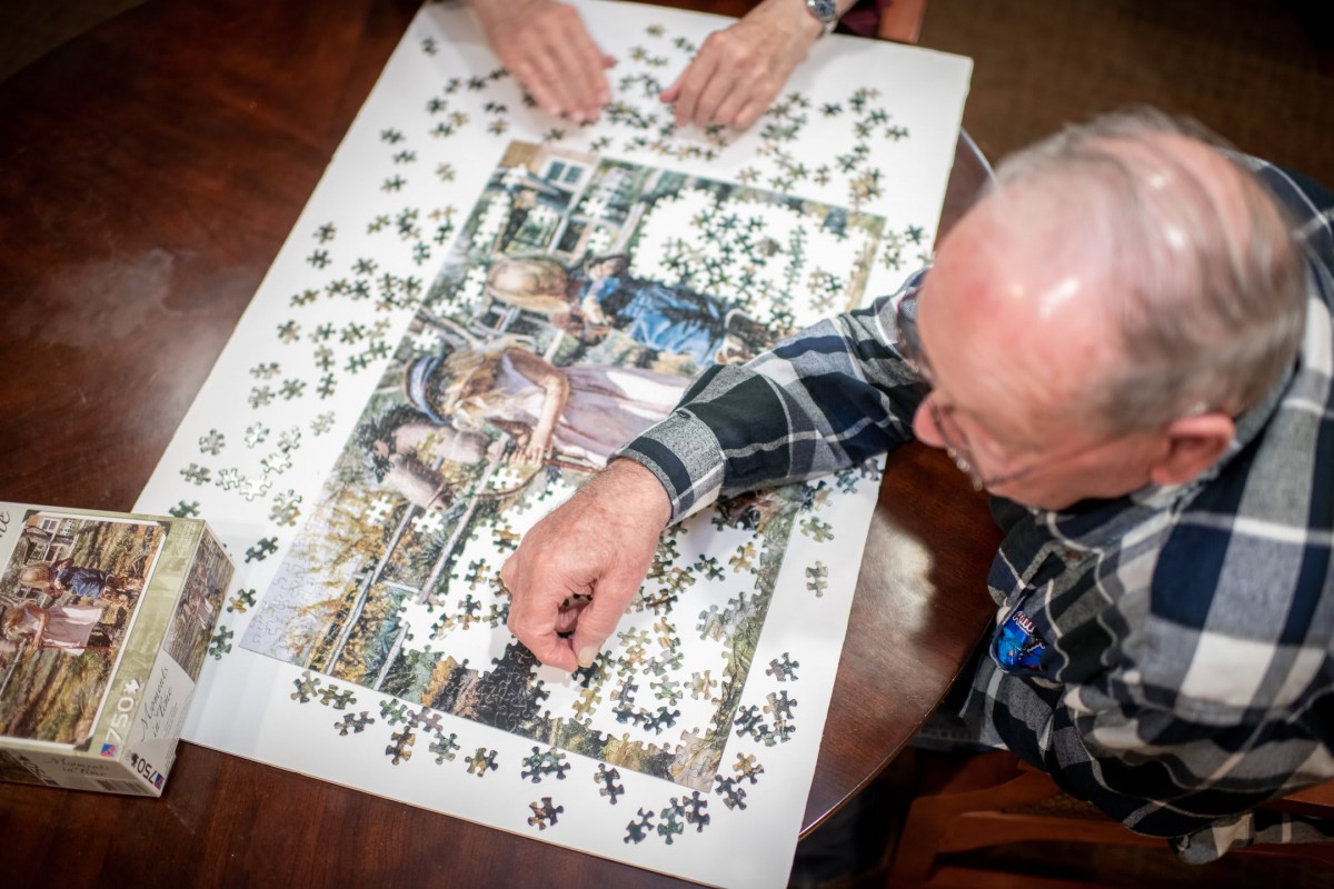 Elderly individuals working together on a jigsaw puzzle at a table.