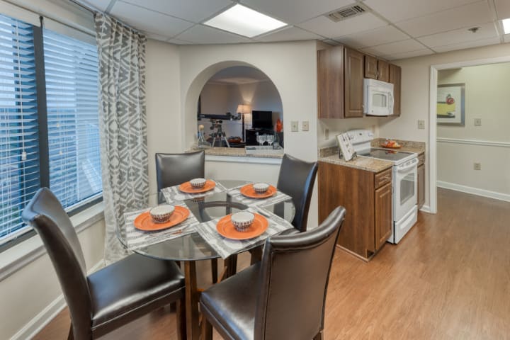 A modern kitchen with a connected dining area, featuring a glass table set with orange-accented place settings.
