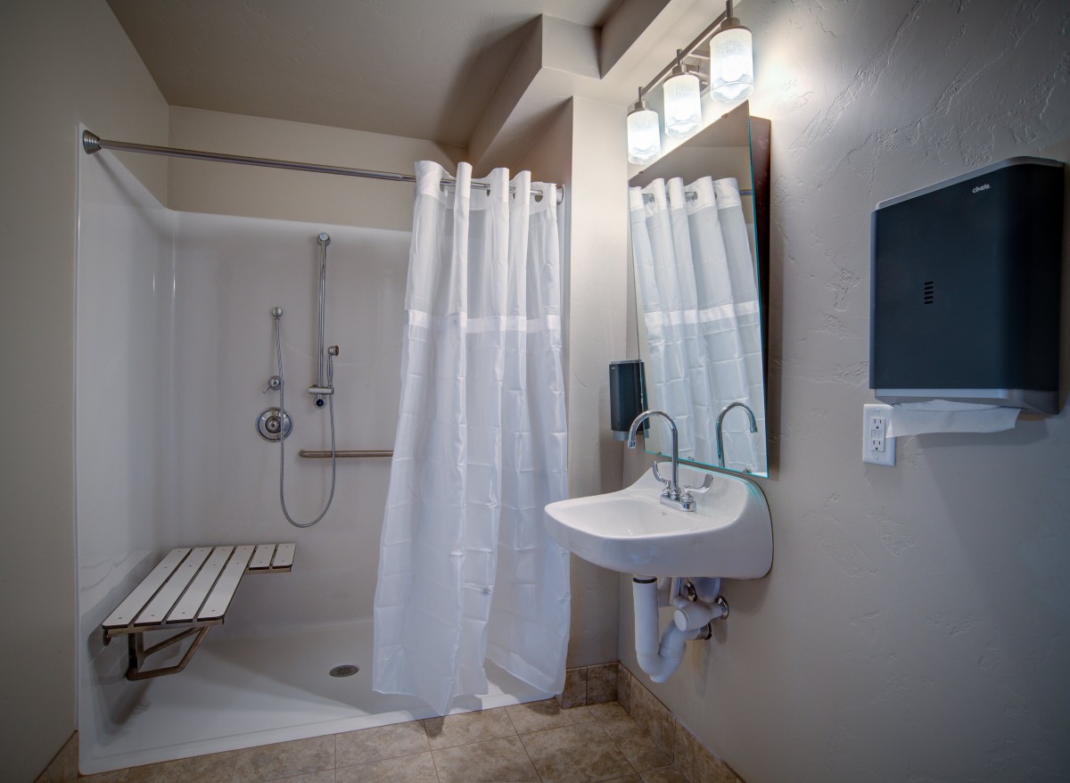 An accessible bathroom featuring a roll-in shower, sink, and handrails.