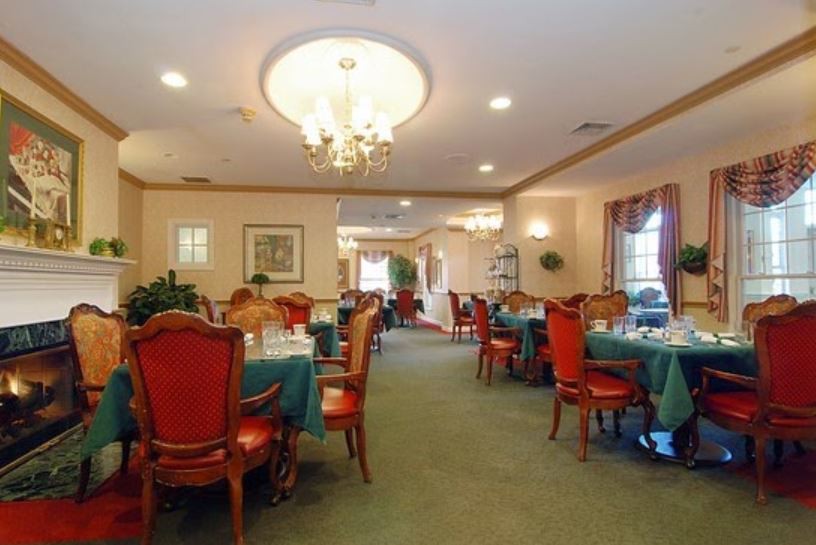 An elegant dining room with a chandelier, set for a meal with tables and red chairs.