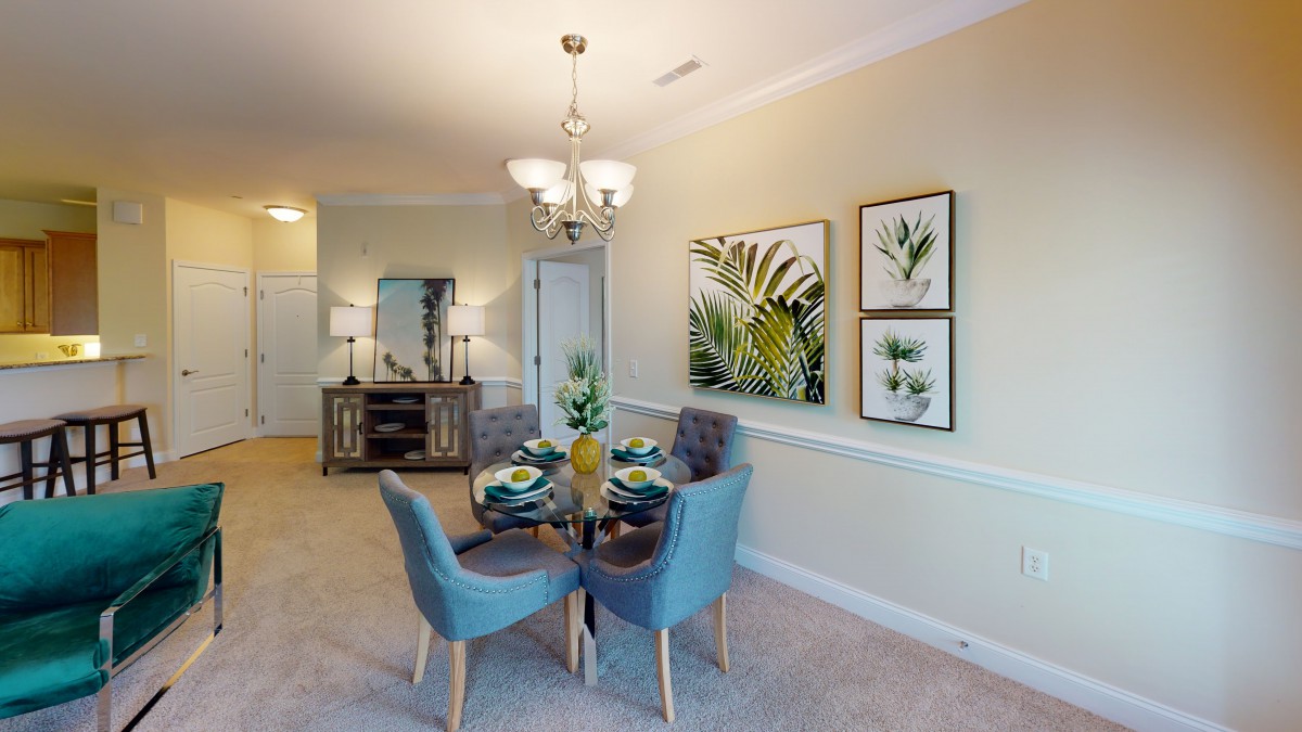 A cozy dining room with blue chairs around a table, elegant chandelier lighting, and botanical artwork adorning the walls.