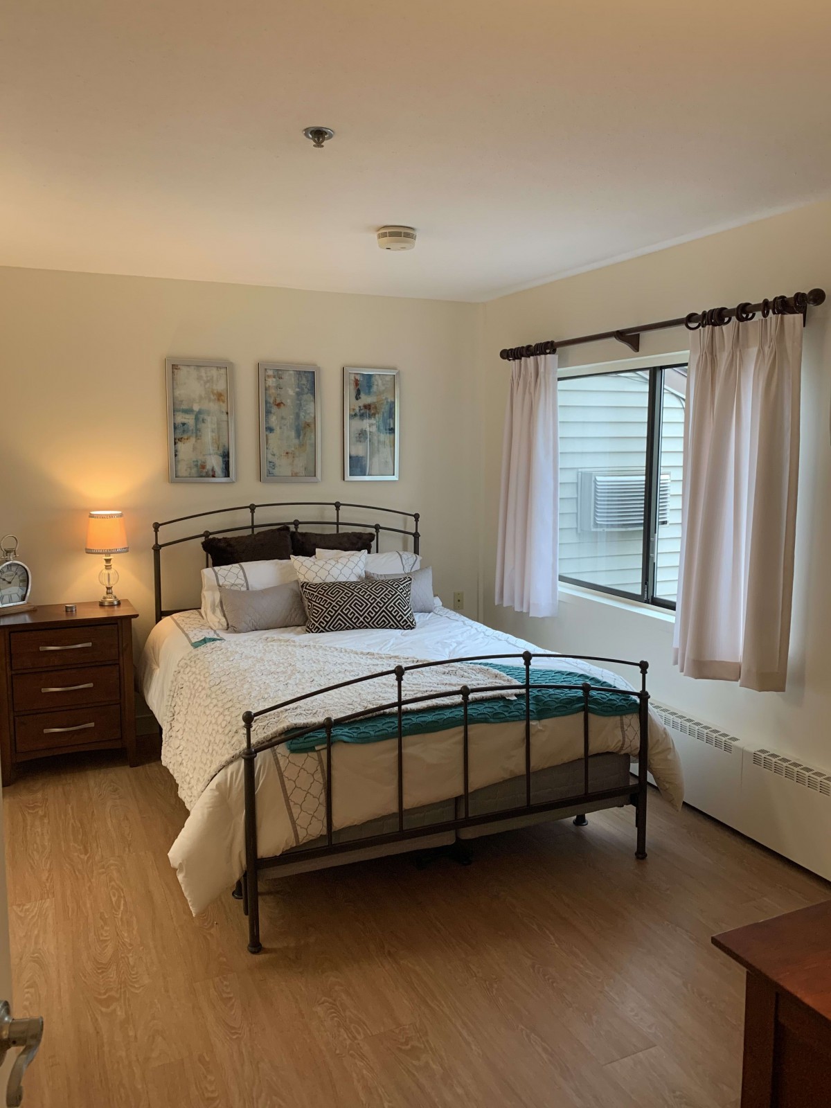 A cozy bedroom with a neatly made bed, nightstand, lamp, and artwork on the wall.