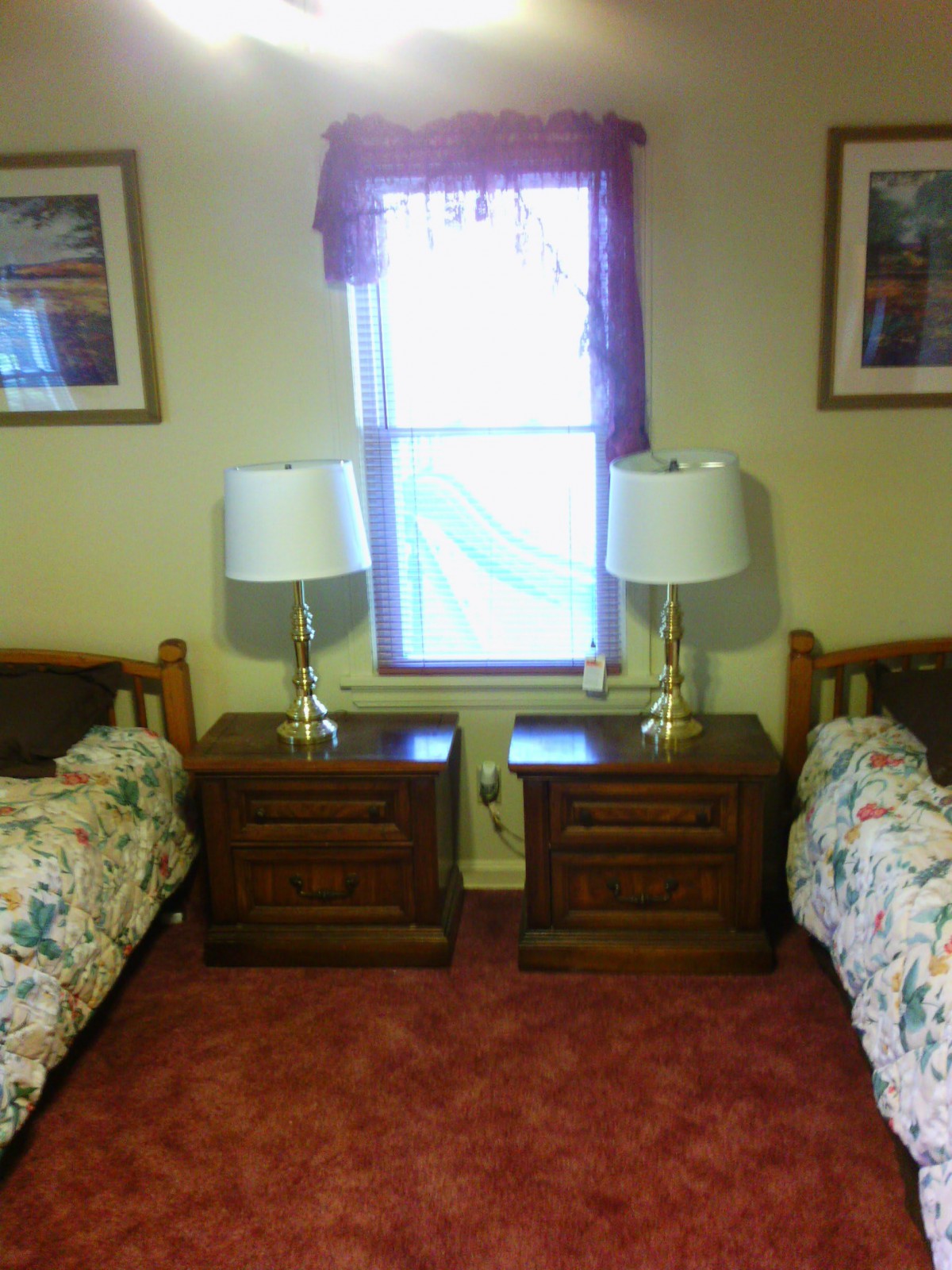 A cozy bedroom with twin beds and matching nightstands, featuring elegant lamps and a central window.