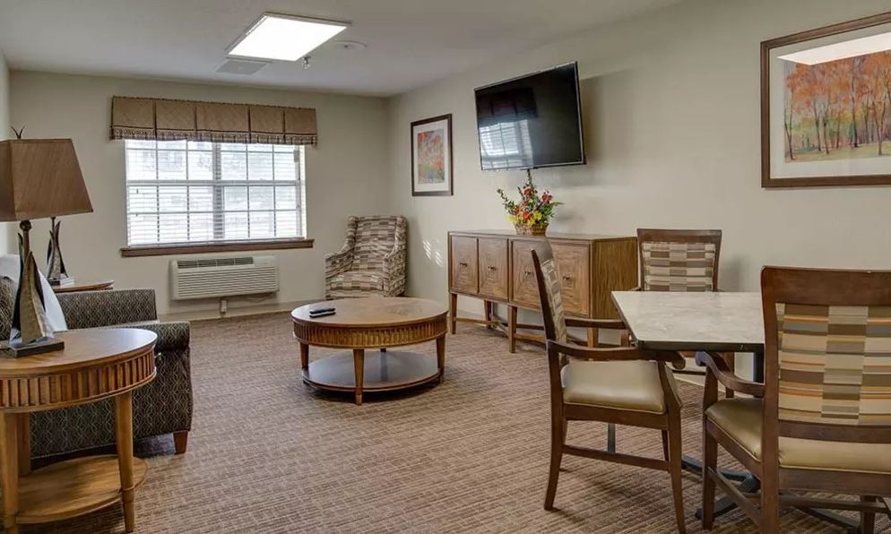 A cozy living room with a television, comfortable seating, and natural light.