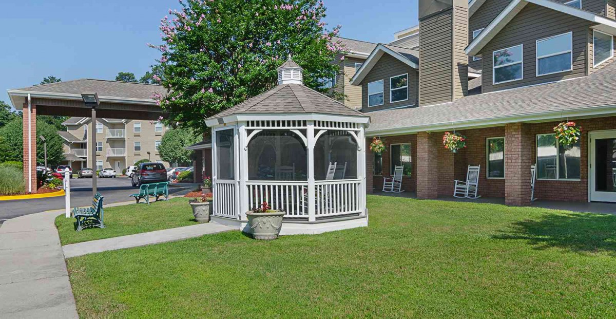 A white gazebo on a green lawn in front of a house.