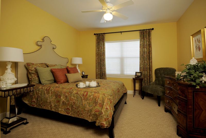 A cozy bedroom with yellow walls, a bed adorned with pillows and a comforter, flanked by curtains, and a chair in the corner.