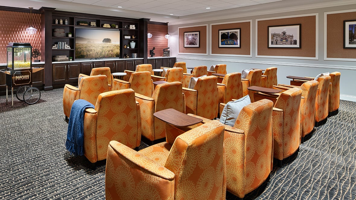 A cozy home theater with orange recliner chairs arranged in rows facing a large screen.