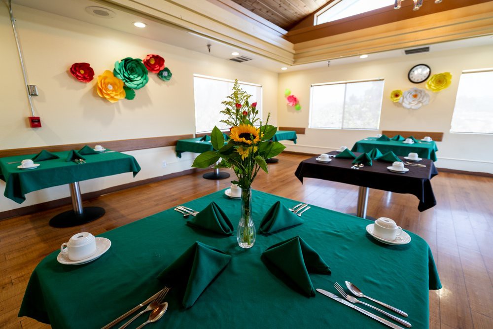 A well-decorated dining room with green tablecloths and flower centerpieces.