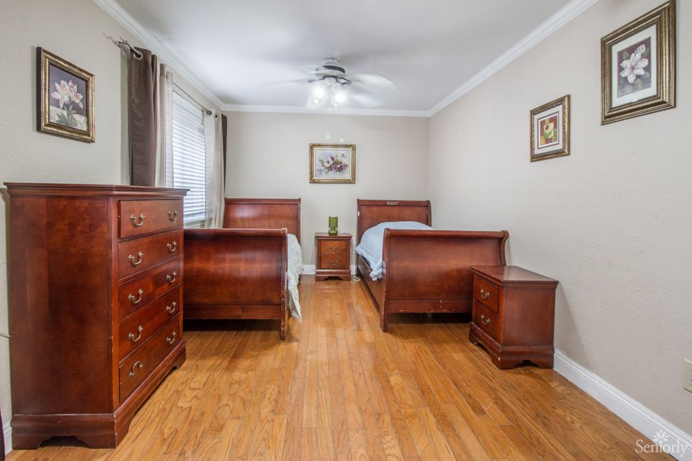 A cozy bedroom featuring twin wooden beds, a dresser, nightstand, and hardwood floors.