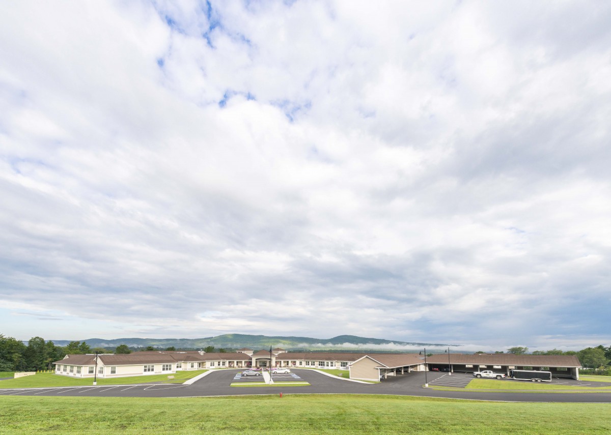 A wide shot of a building complex with a cloudy sky in the background and a parking lot in the foreground.