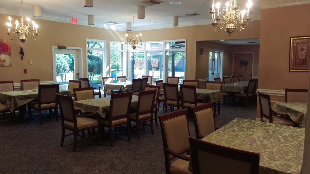 A spacious dining area with multiple tables and chairs, adorned with chandeliers and large windows allowing natural light.