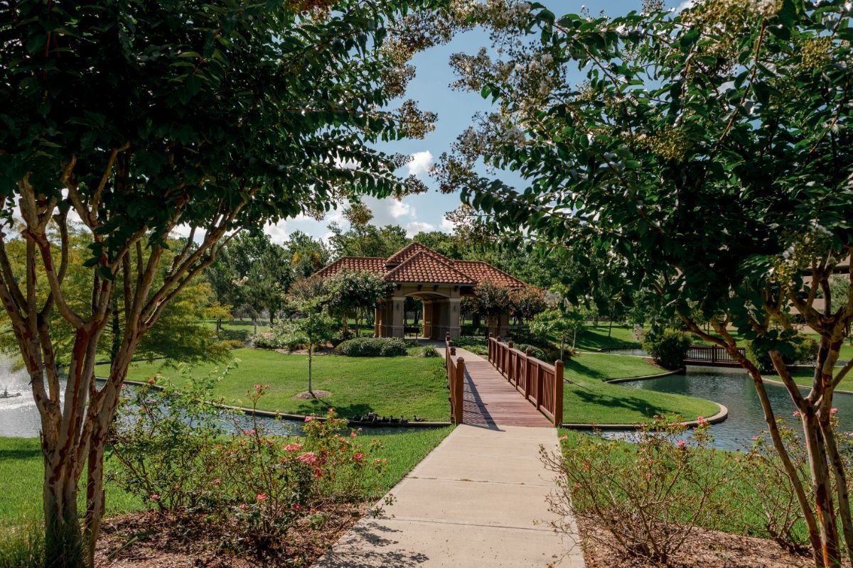 A serene garden with a wooden bridge leading to a house surrounded by lush greenery.