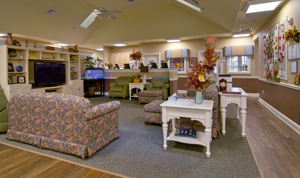 A cozy living room with floral sofas, a carpeted floor, and decorative tables.