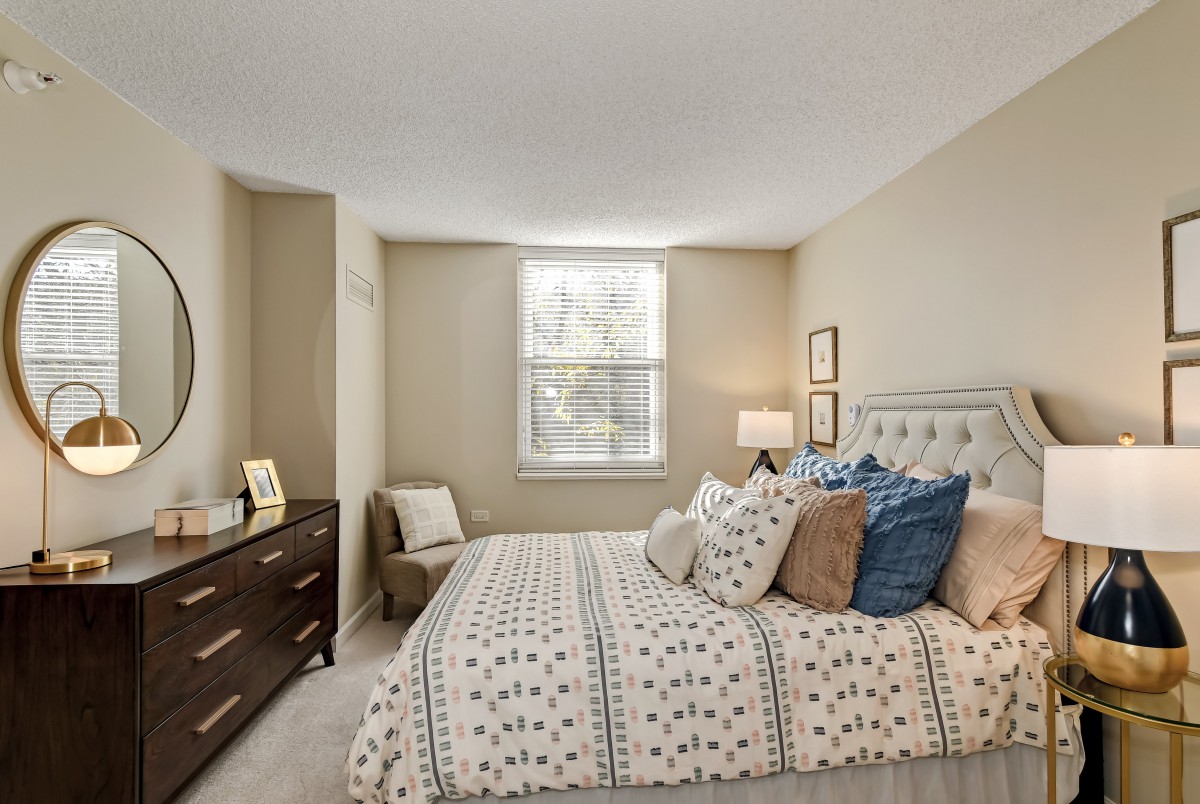 A cozy bedroom featuring a bed with decorative pillows, a dresser, and soft lighting.