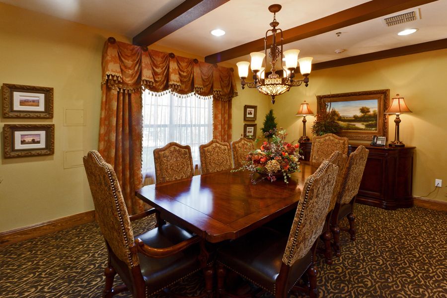 A traditionally styled dining room featuring a wooden table and upholstered chairs, with an elegant chandelier and rich drapery.