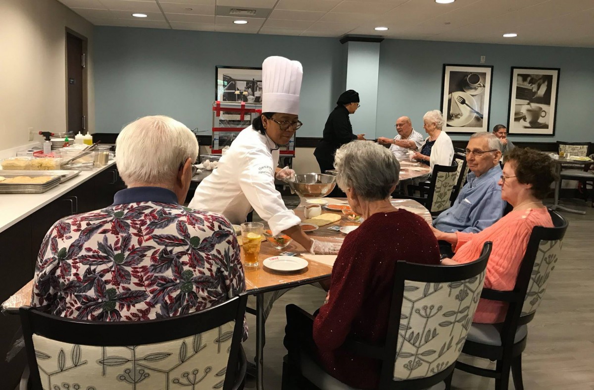 A chef serves a group of seniors at a restaurant table.