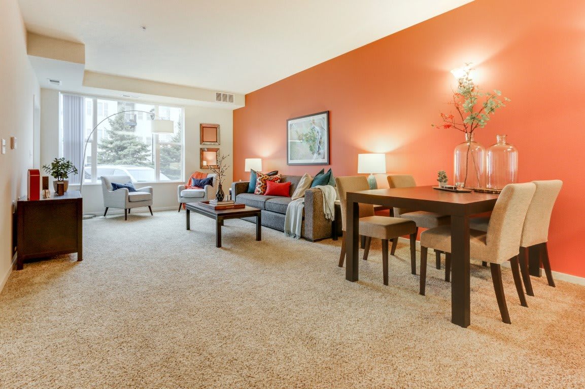 A warmly decorated living room with an orange accent wall, featuring a comfortable sofa and a dining area.