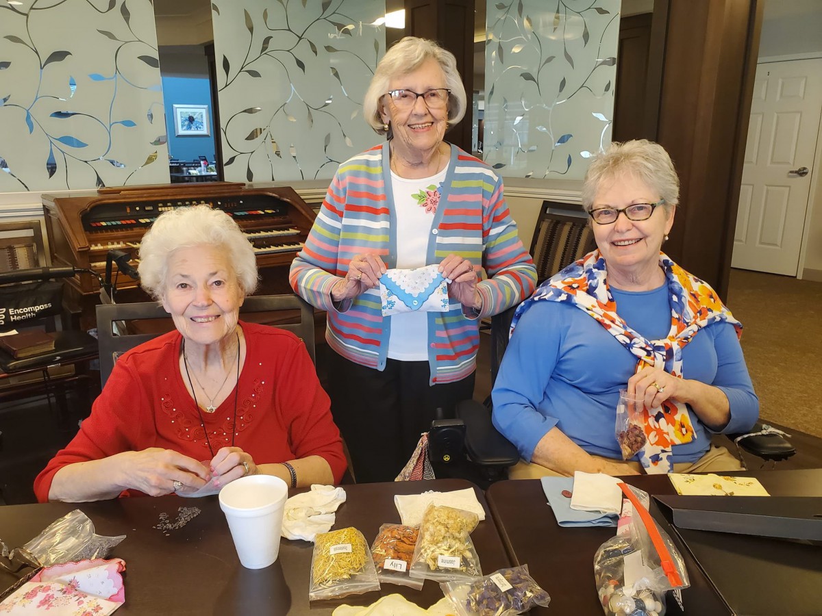 A group of elderly women enjoying snacks and crafts at a table indoors.