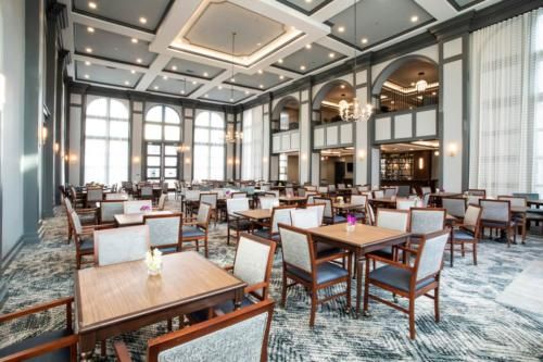 An elegant dining area with neatly arranged tables and chairs, featuring large windows and sophisticated lighting.