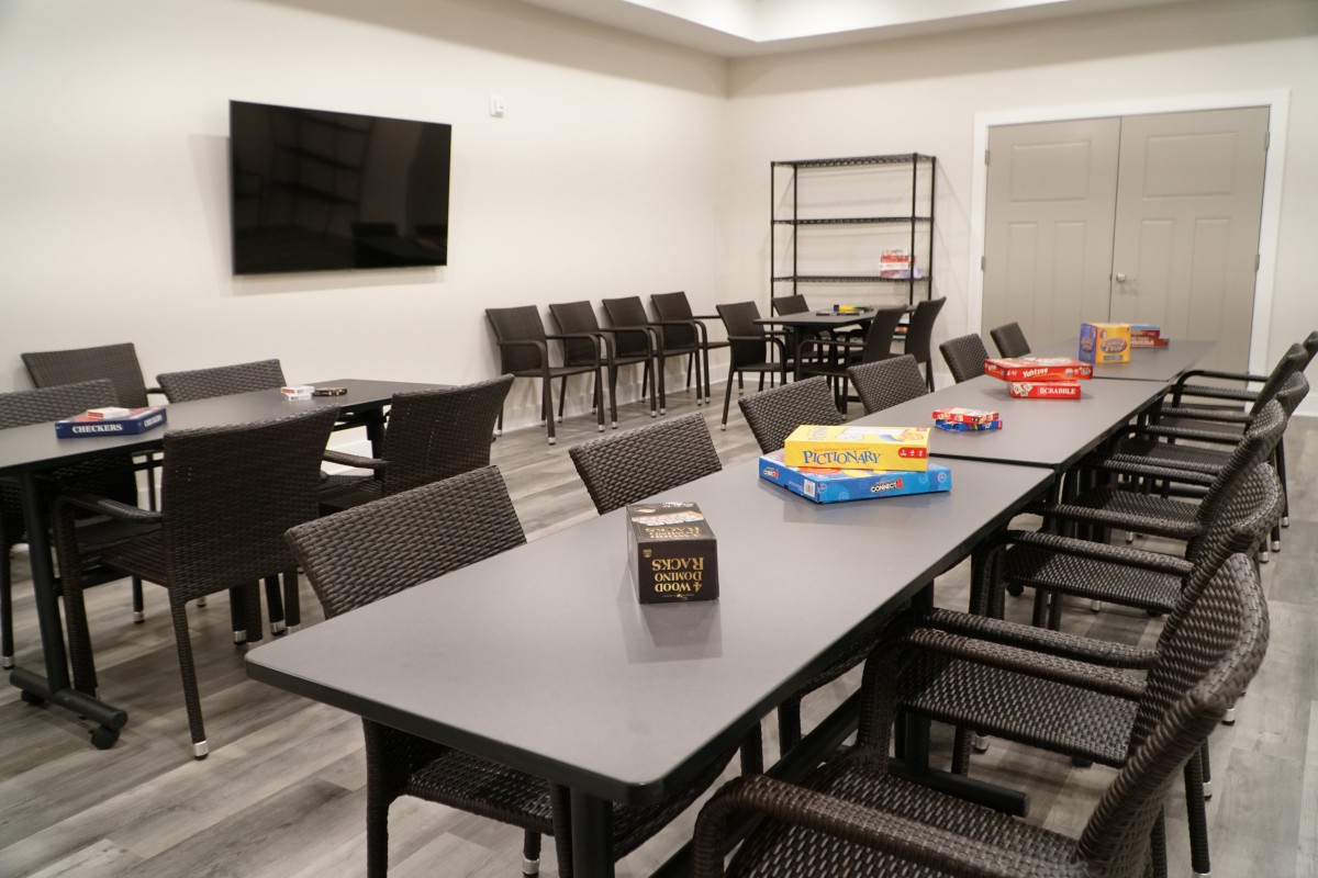 A well-lit conference room with tables and chairs, featuring board games and a large television on the wall.