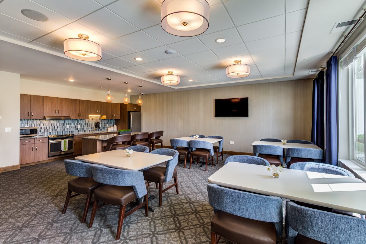 A modern conference room with multiple tables and chairs, featuring stylish lighting fixtures and a wall-mounted television.