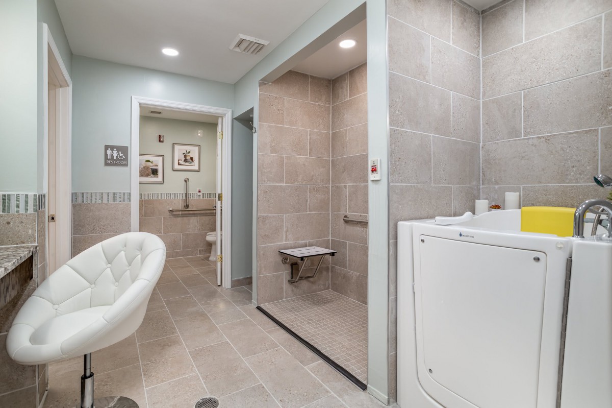 A modern bathroom with a walk-in shower, washer, and seating area.