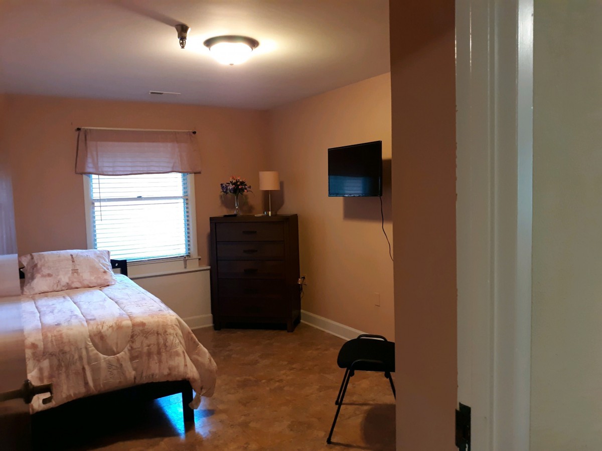 A cozy bedroom with a bed, dresser, and wall-mounted TV.