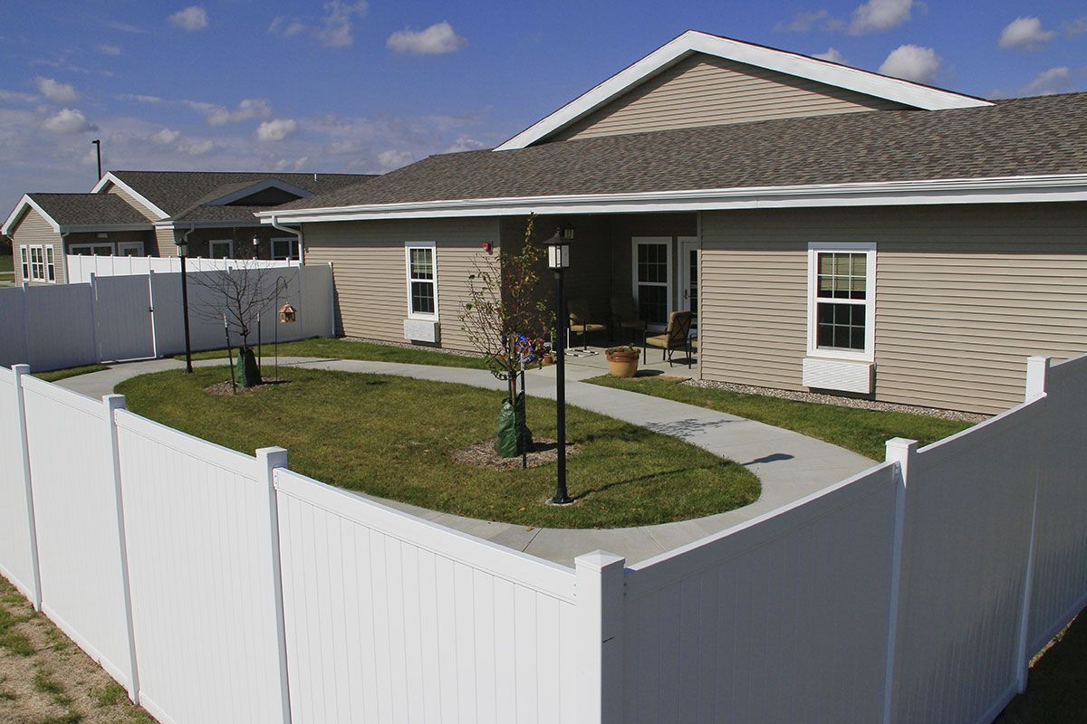 A cozy backyard with a white fence surrounding a well-maintained lawn and patio area.