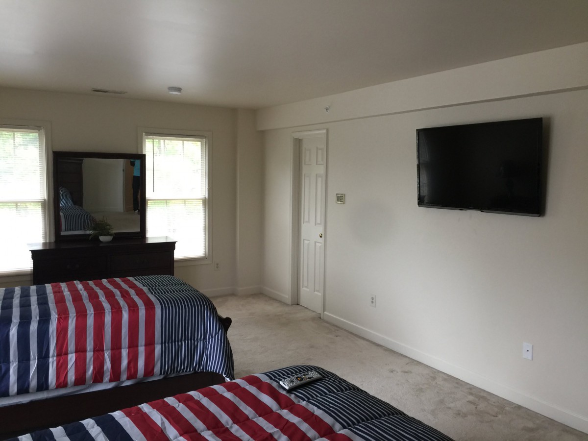 A bedroom with two beds, a wall-mounted TV, and a window.