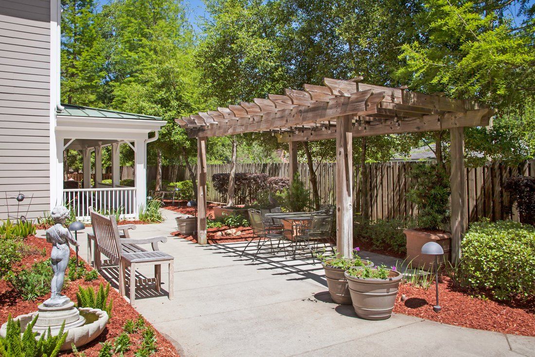 A beautiful garden features a wooden pergola and a gazebo, surrounded by lush greenery and outdoor seating.