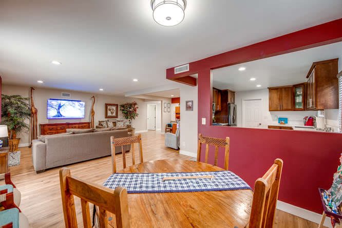 An open-concept home interior featuring a dining area, living room with a TV, and kitchen with hardwood flooring.