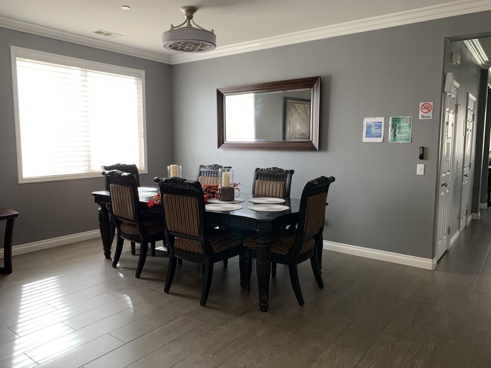 A dining room with a dark wooden table and chairs, a large mirror on the gray wall, and a modern chandelier overhead.