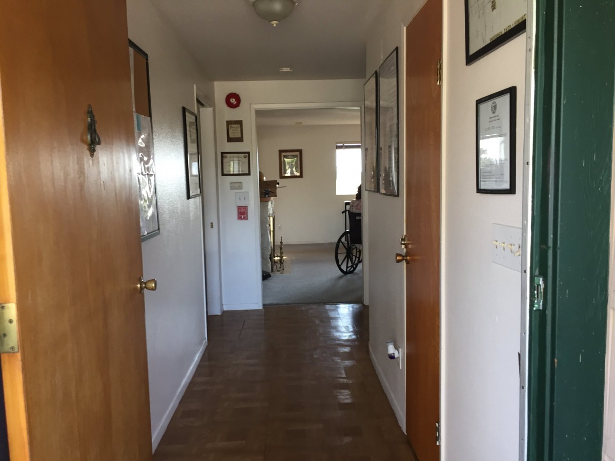 A hallway with wooden floors, several doors, and a bicycle at the end.