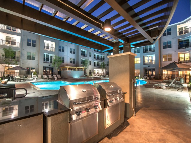 Modern apartment complex with illuminated pool and outdoor grill area at night.